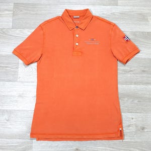 Peut inclure: Polo orange à manches courtes avec un col. Il présente une patte de boutonnage à trois boutons et un petit écusson brodé sur la poitrine. Un écusson drapeau est sur la manche gauche. Le tissu est doux et respirant.