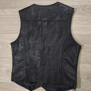 May include: Black leather vest with a classic design. The vest features a V-neck, a tailored fit, and a smooth, textured surface. The back of the vest has a panel design with vertical seams. The vest is a versatile piece of apparel.