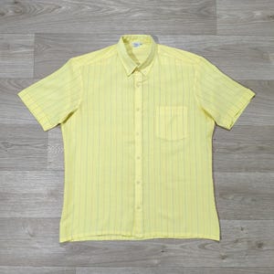 May include: A short-sleeved yellow shirt with vertical blue stripes. The shirt has a button-down collar, a single chest pocket, and a buttoned front closure. The shirt is made of a lightweight fabric.