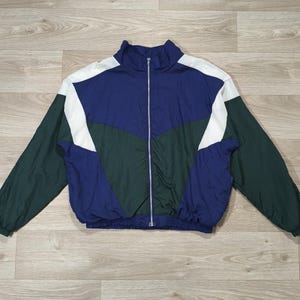 May include: A long-sleeve zip-up track jacket featuring a color-blocked design in navy blue, dark green, and white. The jacket has a high collar, a full-length silver-tone front zipper, and elasticized cuffs and hem for a secure fit.