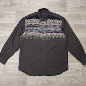 Peut inclure: Chemise à manches longues marron foncé avec un motif ornemental sur la poitrine et les épaules. Le motif comprend des touches de beige, de violet et de vert d'eau. La chemise a un col classique et des poignets boutonnés. Le tissu est texturé.
