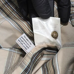 May include: A close-up shot of a tan and brown plaid shirt with a button and a tag. The tag reads "RIP CURL product" and "This label is the guarantee you've bought an original RIP CURL product." The shirt has a classic plaid pattern and is made of a soft fabric.