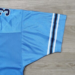 May include: Pale blue jersey with white and navy stripes on the sleeve. The jersey features a mesh panel and a navy number with a white outline. The jersey is made of a smooth, shiny fabric.