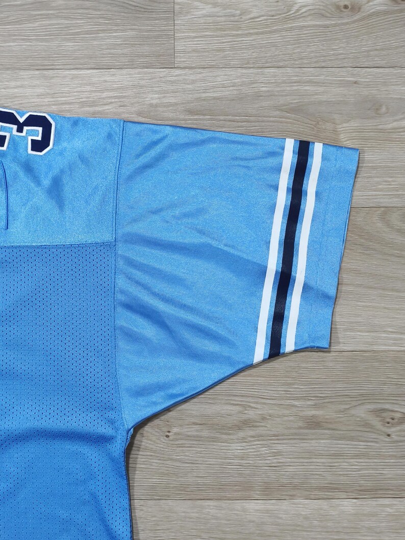 May include: Pale blue jersey with white and navy stripes on the sleeve. The jersey features a mesh panel and a navy number with a white outline. The jersey is made of a smooth, shiny fabric.