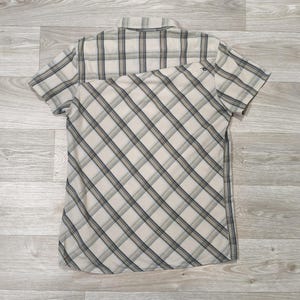 May include: Short-sleeved shirt with a beige, grey, and navy blue plaid pattern. The shirt features a classic collar and a diagonal plaid design on the lower half. The fabric looks lightweight, suitable for warmer weather. Measurements are in cm.