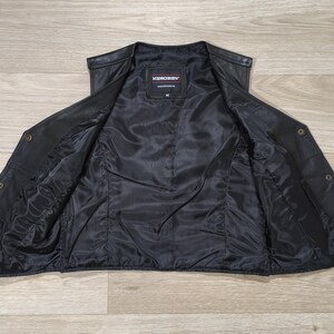 May include: Black leather vest with a satin lining, open to display the interior. The vest has a V-neck, button closures, and a label that reads "KONDORON". The vest is laid flat on a light wood grain surface.