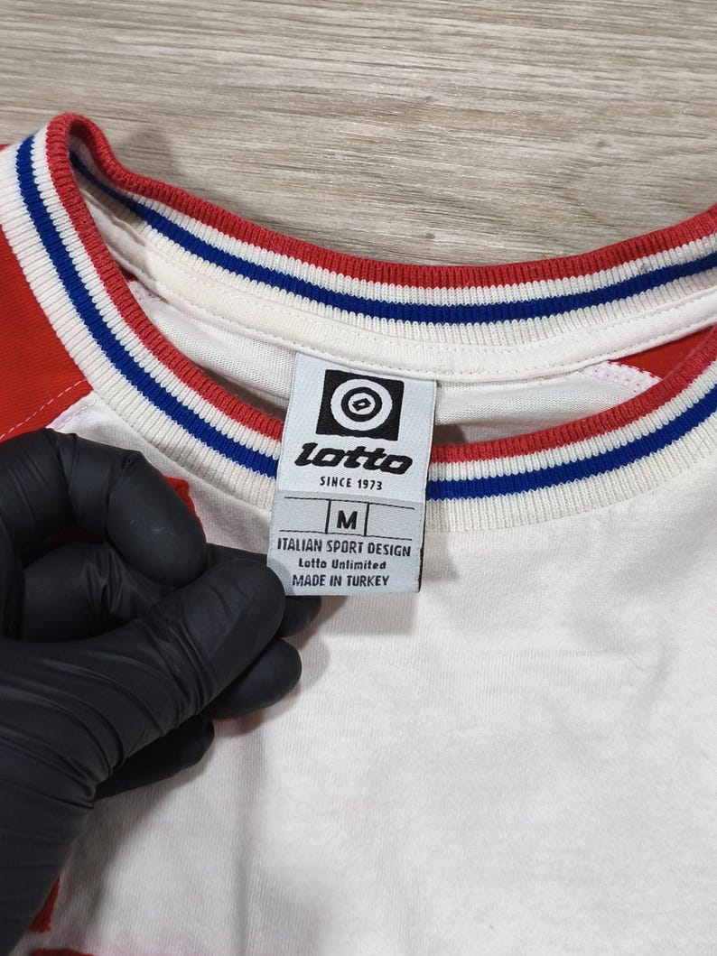 May include: White and red athletic shirt with blue and red trim around the collar. The shirt has a tag that reads "lotto" and "Italian Sport Design". The shirt is a size medium.
