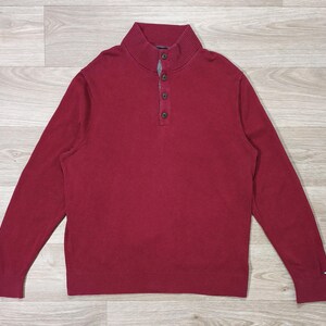 Peut inclure: Un pull à manches longues bordeaux avec un col boutonné. Le pull a un ourlet et des poignets côtelés. Le logo Tommy Hilfiger est visible sur le poignet gauche. Le pull est en matière douce et confortable.