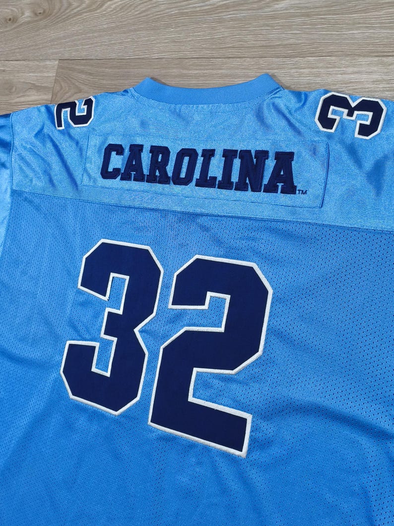 May include: Pale blue mesh jersey with the word "CAROLINA" in navy blue across the chest. The number "32" is in navy blue with a white outline. The jersey has navy blue numbers on the shoulders.