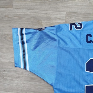 May include: Pale blue jersey with white and black stripes on the sleeve. The jersey features the number "2" in white and navy blue, and the letter "C". The fabric has a mesh texture.
