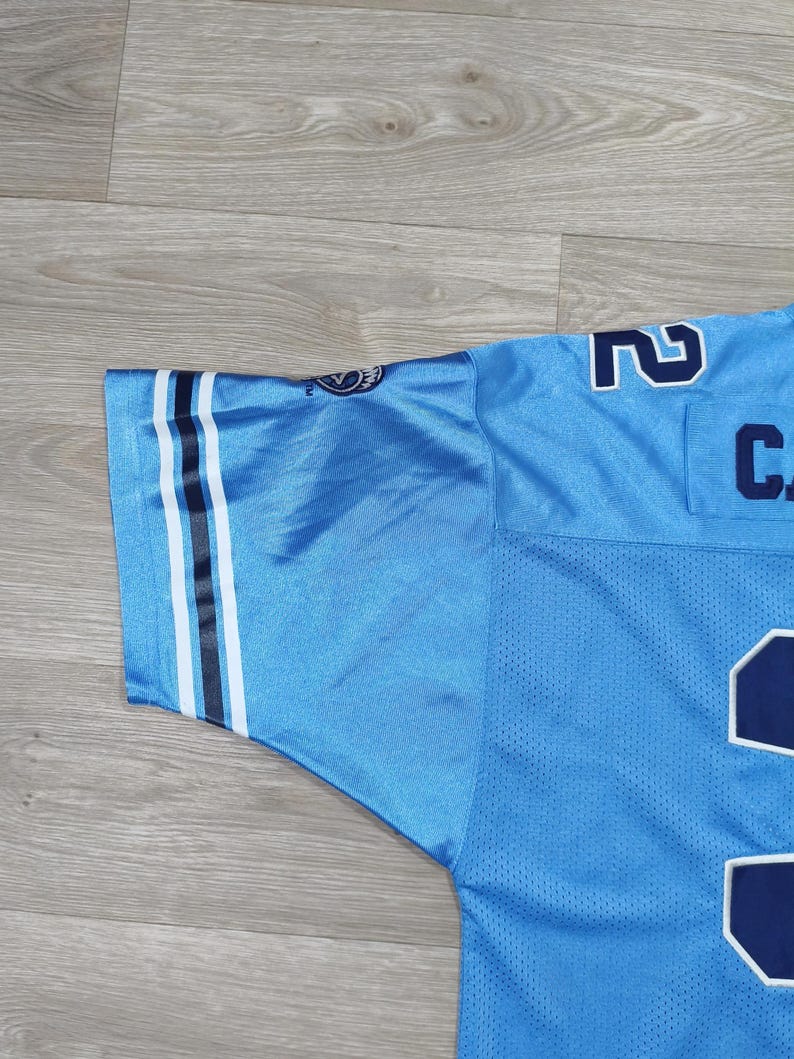 May include: Pale blue jersey with white and black stripes on the sleeve. The jersey features the number "2" in white and navy blue, and the letter "C". The fabric has a mesh texture.