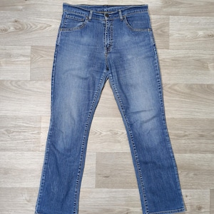 Peut inclure: Un jean en denim bleu délavage moyen doté d'une coupe classique à cinq poches, d'une fermeture à bouton et à glissière, de passants de ceinture à la taille et de légères marques d'usure sur les hanches avec des jambes droites.