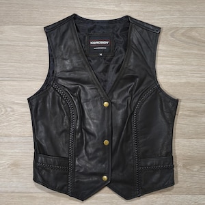 May include: Black leather vest with gold-colored buttons and braided trim. The vest has a V-neck and two front pockets. The brand name "KOROZAN" is visible on the label inside the vest.