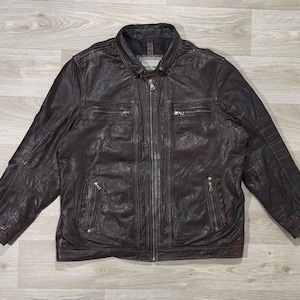 Könnte beinhalten: Braune Lederjacke mit Reißverschluss, mehreren Taschen und einem Kragen. Die Jacke hat eine strukturierte Optik und ein klassisches Design, geeignet für verschiedene Anlässe.