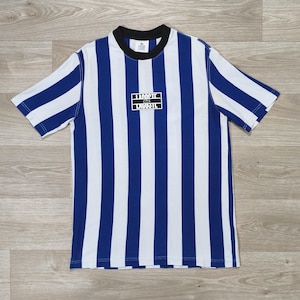 May include: A short-sleeved t-shirt with vertical blue and white stripes. The shirt has a black collar and a rectangular logo with the text "LACOSTE" in white. The shirt is made of a soft, comfortable material.