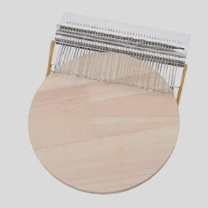 May include: A kalimba instrument with a light wood soundboard and a metal tine bar. The round soundboard is made of light-colored wood. The metal tines are arranged above the soundboard. The instrument has a silver metal bar and a wooden frame.