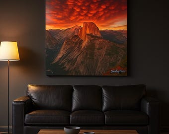 Könnte beinhalten: Ein großer Leinwanddruck einer Berglandschaft unter einem feurigen roten und orangen Sonnenuntergang. Das Bild zeigt eine markante Felsformation und einen dramatischen Himmel. Der Druck wird über einem schwarzen Ledersofa angezeigt.