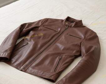 May include: A brown leather jacket with a stand-up collar and several zipped pockets. The jacket is displayed on a white bedspread. It features a front zip and long sleeves.
