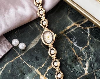 Relógio feminino elegante e delicado com pulseira dourada e pérolas brancas.