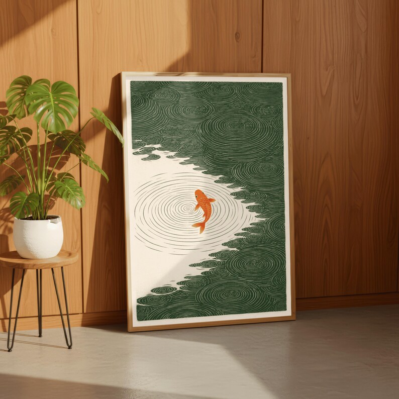 K&ouml;nnte beinhalten: Gerahmter Kunstdruck mit einem orangefarbenen Koi-Fisch, der in einem Teich mit gr&uuml;nem Wasser und kreisf&ouml;rmigen Mustern schwimmt. Das Kunstwerk hat einen minimalistischen Stil mit cremefarbenem Hintergrund und Holzrahmen. Der Druck lehnt an einer Holzwand.