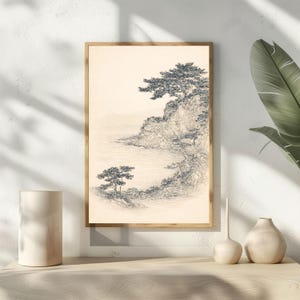 May include: A framed black and white landscape art print. The artwork depicts a coastal scene with trees, cliffs, and water. The print is in a light-colored wooden frame, creating a serene and natural aesthetic. The art piece is displayed on a light-colored wooden surface.