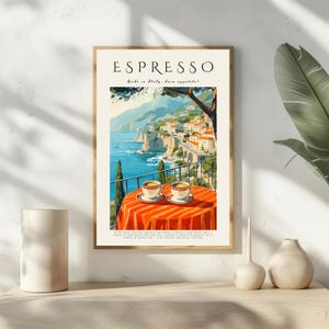 May include: Framed art print with the word "Espresso" at the top. The image depicts a coastal Italian landscape with two cups of coffee on a red and orange striped table. The print is in a light wood frame, evoking a cafe setting.