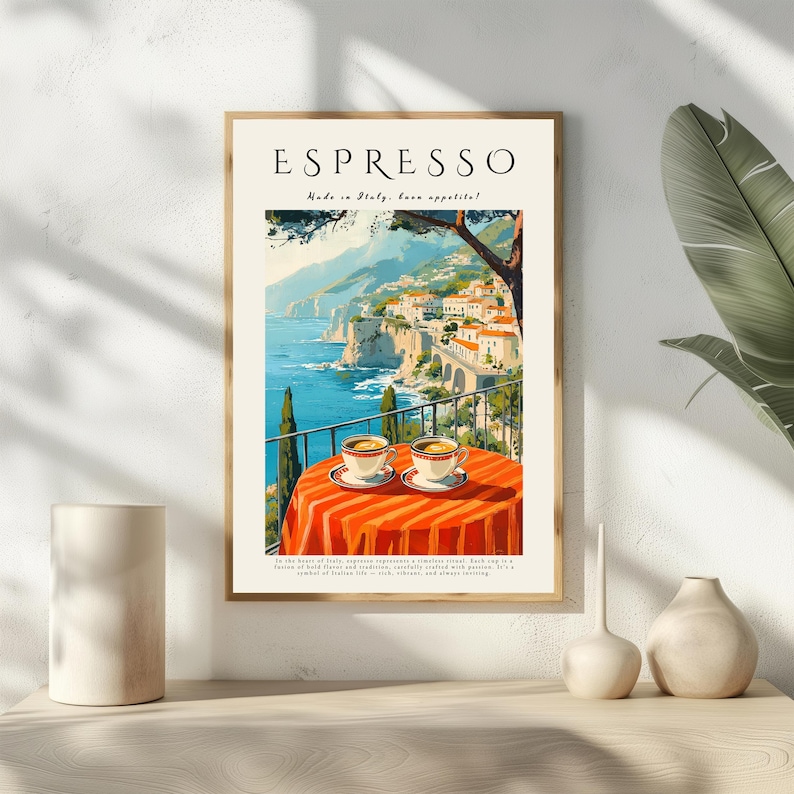 May include: Framed art print with the word "Espresso" at the top. The image depicts a coastal Italian landscape with two cups of coffee on a red and orange striped table. The print is in a light wood frame, evoking a cafe setting.