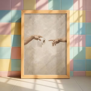 Puede incluir: Obra de arte enmarcada que representa una parodia de 'La Creaci&oacute;n de Ad&aacute;n' de Miguel &Aacute;ngel, con dos manos extendi&eacute;ndose hacia un rollo de papel higi&eacute;nico. La obra est&aacute; en un marco de madera clara, sobre un fondo neutro.