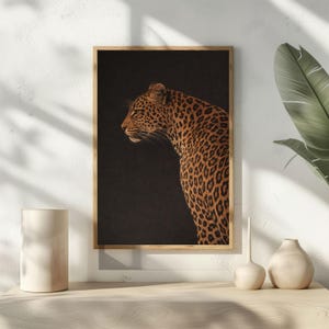 Peut inclure: Impression encadrée d'un léopard de profil sur fond noir. Le pelage du léopard est tacheté de brun et de beige. Le cadre est en bois clair, et l'impression est présentée sur une surface blanche, créant un contraste saisissant.