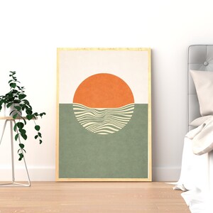 Könnte beinhalten: Abstrakter Kunstdruck mit einer orangefarbenen Sonne über einem wellenförmigen, gestreiften Design in Grün. Die obere Hälfte ist cremefarben. Das Kunstwerk ist in einem hellen Holzrahmen gerahmt, geeignet für die Inneneinrichtung.
