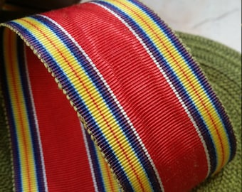 Puede incluir: Cinta roja, amarilla, azul y blanca a rayas. La cinta está tejida con un patrón texturizado.