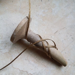 May include: A wooden shoe last with gold ribbon wrapped around it. The ribbon is woven in a crisscross pattern around the pointed end of the last. The wooden last is light brown and has a smooth finish.