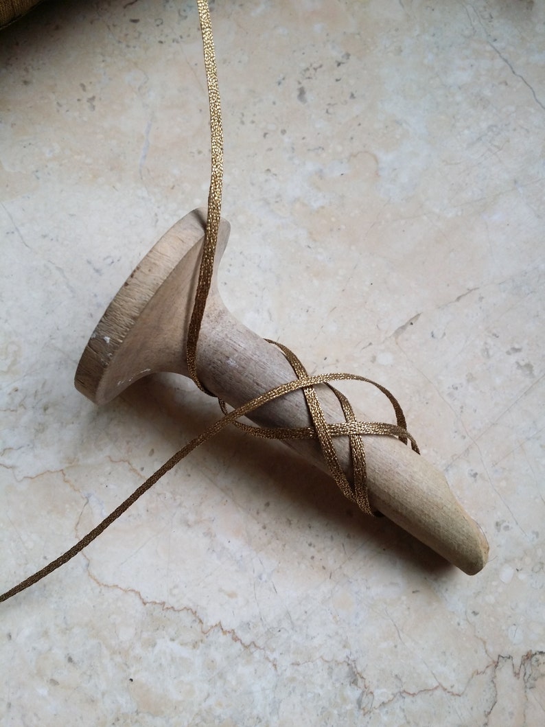 May include: A wooden shoe last with gold ribbon wrapped around it. The ribbon is woven in a crisscross pattern around the pointed end of the last. The wooden last is light brown and has a smooth finish.