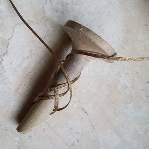May include: A wooden shoe last with gold ribbon wrapped around it. The last is a light beige color, and the ribbon is a metallic gold. The ribbon is wrapped in a crisscross pattern around the last.