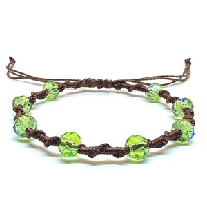 May include: A handmade bracelet featuring vibrant green faceted beads strung on a dark brown cord. The adjustable cord allows for a comfortable fit. The bracelet is displayed on a white background.