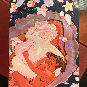 May include: Art print featuring two figures in a celestial scene. One figure has light pink hair and skin, the other has dark hair and reddish skin. The background is dark blue with stars and iridescent accents.