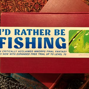 Könnte beinhalten: Ein rechteckiger Aufkleber mit dem Text "I'D RATHER BE FISHING" in Blau. Der Aufkleber enthält auch den Text "IN CRITICALLY ACCLAIMED MMORPG FINAL FANTASY XIV NOW WITH EXPANDED FREE TRIAL UP TO LEVEL 70" und eine Fischillustration.