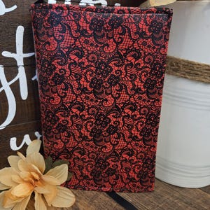 May include: A red and black lace-patterned book cover. The cover is a vibrant red with an intricate black lace design. A black ribbon bookmark is visible. The book cover is standing upright.
