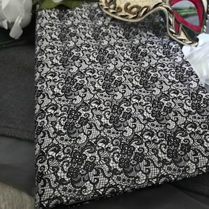 May include: A black and white lace-patterned journal with a black ribbon bookmark. A decorative Venetian mask with gold, black, and red accents rests nearby, along with white flowers. The journal's cover features an intricate lace design.