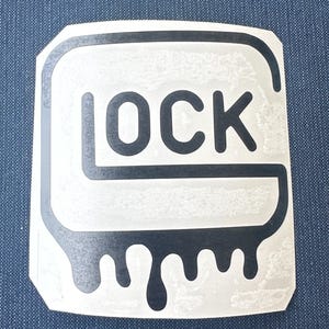 May include: A white sticker with a black outline and the word "OCK" in black block letters. The bottom of the sticker has a dripping design. The sticker is on a blue background.