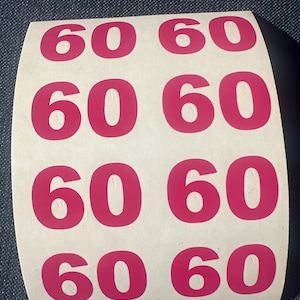 May include: A roll of white stickers with the number "60" printed in bright pink. The stickers are arranged in rows and columns, with the number repeated multiple times across the surface.