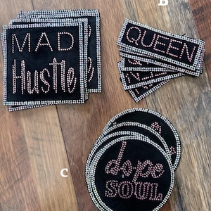May include: Black coasters with rhinestone accents. One set says "MAD Hustle", another says "QUEEN", and a third says "dope soul". The coasters are square and round.