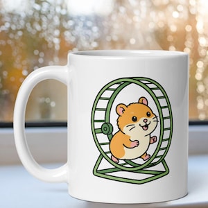 May include: A white ceramic mug featuring a colorful graphic of a light brown hamster running inside a green exercise wheel. The hamster has a cream-colored belly, small ears, and a cheerful expression. The design is centered on the mug's exterior.