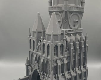May include: A gray, 3D-printed model of a gothic cathedral with a clock tower. The model has intricate architectural details, including arched windows, spires, and a dice tray. Two green dice are visible in the tray.