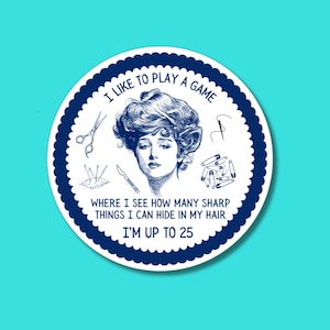 May include: A circular sticker with a dark blue scalloped border on a white background. It features a blue line-art illustration of a person with voluminous hair, surrounded by scissors, a needle, a pincushion, a scalpel, and safety pins.