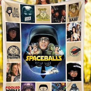 May include: A cream-colored blanket featuring a collage of images and text from the movie "Spaceballs." The central image is a character in a Darth Vader-like helmet. Other squares include characters and quotes like "Evil will always triumph because good is dumb."