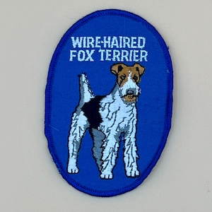 May include: A blue, oval-shaped embroidered patch featuring a Wire-Haired Fox Terrier. The dog is depicted in white, black, and brown. The text "WIRE-HAIRED FOX TERRIER" is embroidered in white above the dog illustration.