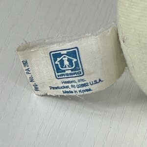May include: Close-up of a white fabric tag with the Hasbro logo, a blue square with a house and dog silhouette. The tag includes the text "Hasbro, Inc. Pawtucket, RI 02862 U.S.A. Made in Korea."