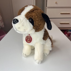 May include: A plush St. Bernard dog toy with brown, white, and black fur. It has a red "Collector's Choice" tag. The toy is sitting on a white surface.