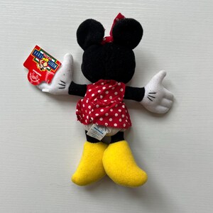 May include: A Minnie Mouse soft toy featuring a red polka dot dress, yellow shoes, and white gloves. The toy has a red bow and black ears. A red tag is attached to the left hand. The tag reads "Mickey's for Kids".